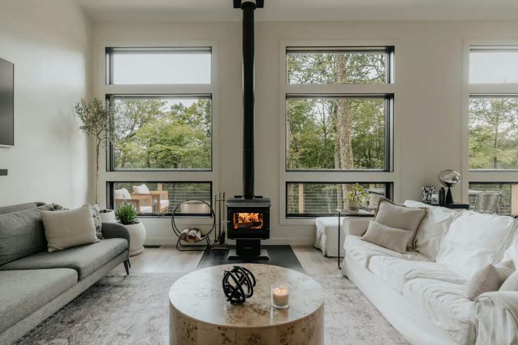 Modern living room with sitting area including sofas with cushions and small table next to fireplace, overlooking patio with trees.